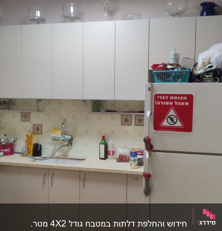 מטבח עם ארונות לבנים, כיור וברז, כלים על השיש